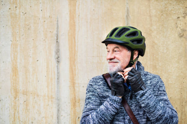 istock Active senior man standing outdoors against a concrete wall, putting on bicycle helmet. 1074966826