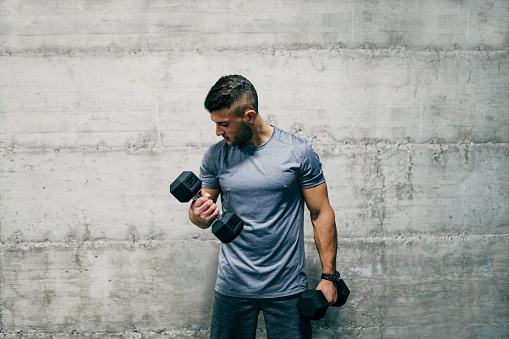 Man standing in front of wall and lifting dumbbells. How many sets is good for biceps?