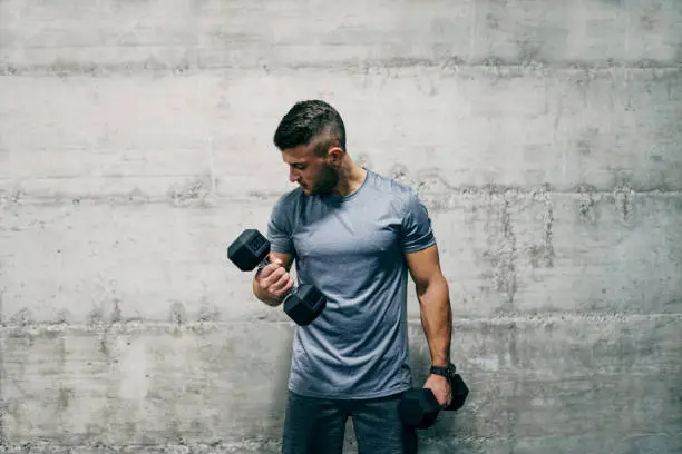 Photo of Man standing in front of wall and lifting dumbbells. How many sets is good for biceps?