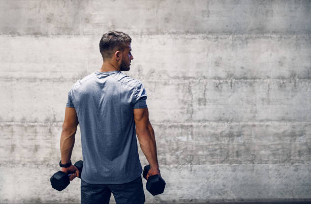 uomo che tiene manubri mentre si trovava con la schiena girata. fit non è una destinazione, è uno stile di vita. - abdominal muscle muscular build barbell bicep foto e immagini stock