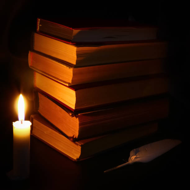 istock old books, burning candle and feather in the dark 1074976870
