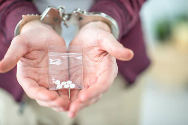 Drug crimes A man's hands are in handcuffs. He is holding a baggie of white pills. recreational drug stock pictures, royalty-free photos & images