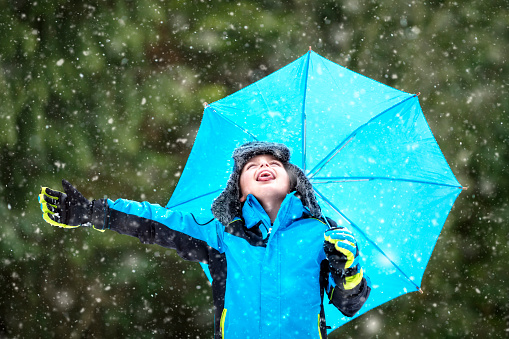 Snow falling on boy in winter with umbrella catching snowflakes on tongue