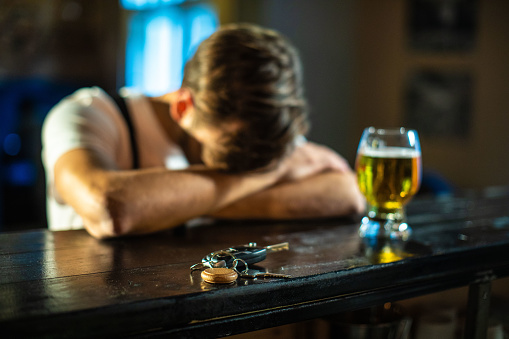 Handsome Man With Head In Hands Standing Drunk At Bar with car keys on the table