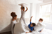 large group of friends taking goog time on bed with pillow fight