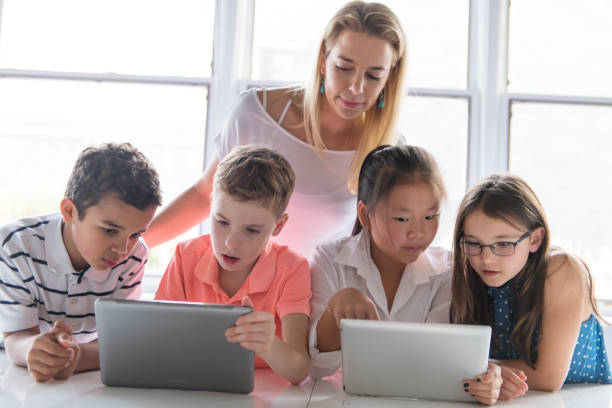 istock child with technology tablet and laptop computer in classroom teacher on the background 1074987322