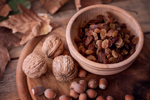 Raisin - dried grape fruits in wood bowl with walnut and hazelnut at wooden autumn background. Close-up, selective focus
