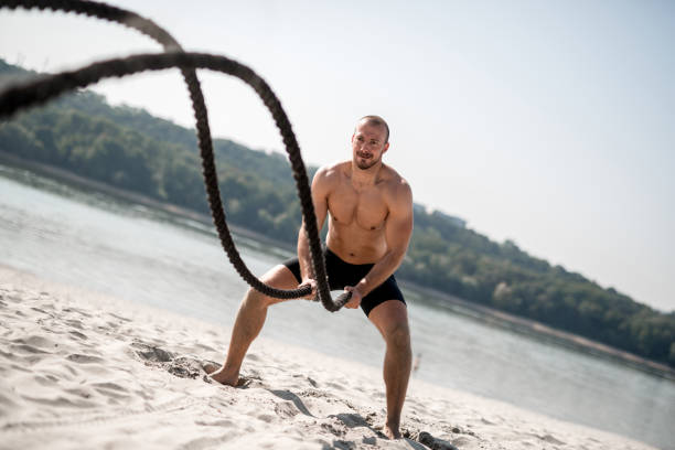 hombre fuerte haciendo ejercicios con la cuerda de la batalla - abdomen abdominal muscle muscular build beautiful fotografías e imágenes de stock