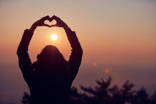 istock Girl making heart - shape sign with hands at sunset / sunrise time. 1075002924