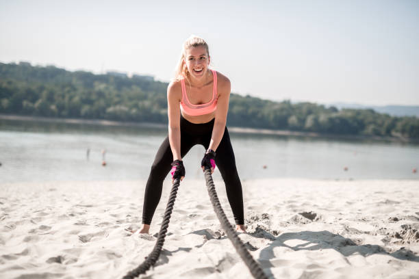 Happy women athlete doing battle rope workout. Exercising on a sunny day.
