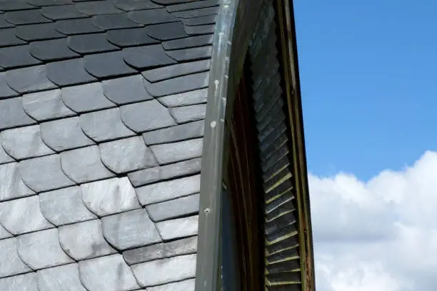 grey natural slate covered curved roof detail with wood trim and blue sky