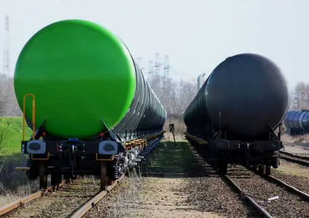 green and black oil tanker cars in train station in diminishing perspective with industrial background