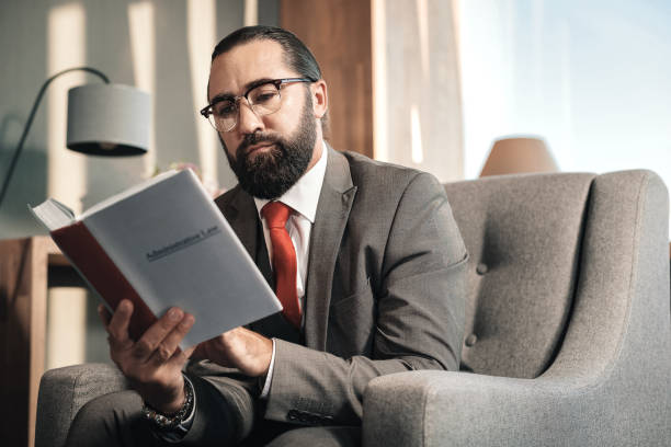 istock Bearded smart advocate wearing red tie reading administrative law 1075011768