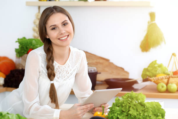 istock Young  woman using tablet while cooking or making online shopping in kitchen. Girl looking at the camera. Healthy lifestyle and vegan meal concepts 1075017112