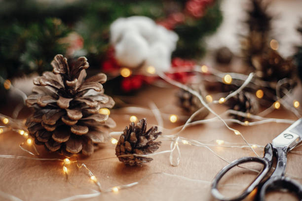 istock Pine cones, fir branches, wreath, red berries, thread, scissors, cinnamon, cotton, lights on rustic wooden background. Details for making christmas wreath at workshop. Atmospheric image 1075036692
