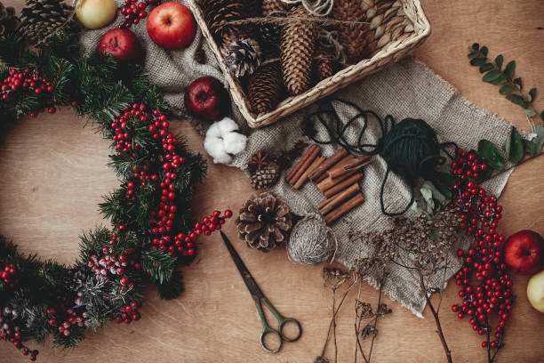 istock Rustic Christmas wreath, flat lay. Fir branches with red berries,pine cones,ribbon, scissors, cinnamon, cotton, apples on rustic wood. Atmospheric moody image at holiday workshop 1075036912