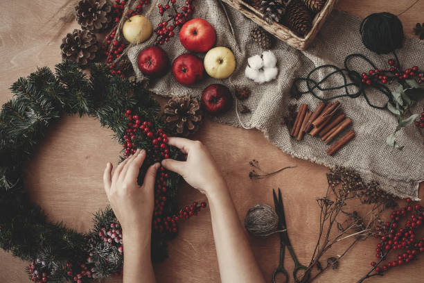 istock Hands holding fir branches, red berries and pine cones,thread, scissors, cinnamon, cotton on rustic wooden background. Rustic Christmas wreath flat lay. Making  wreath at workshop 1075039164