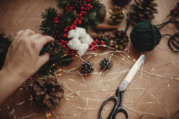 istock Fir branches, wreath, red berries, pine cones, thread, scissors, cinnamon, cotton, lights on rustic wooden background. Details for making christmas wreath at workshop. Atmospheric image 1075040156