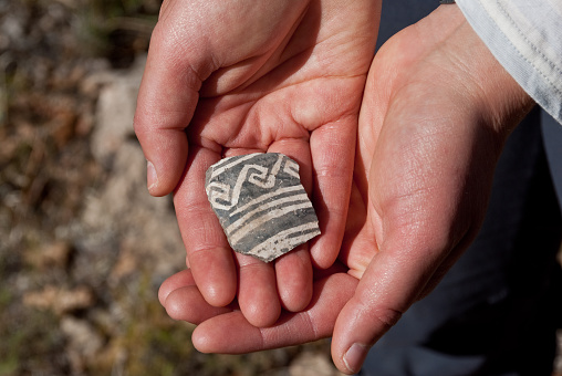 Nearly a thousand years ago natives inhabited the lower elevations around the San Francisco Peaks of Arizona. In an area so dry it would seem impossible to live, they built pueblos, harvested rainwater, grew crops and raised families. Today the remnants of their villages dot the landscape along with other artifacts. Decorated pottery such as the shard shown in the picture was likely not produced in the area where the shard was found. This type of pottery was brought in for trading purposes by people from nearby tribes. It is unlawful to remove shards from an archeological site. They may be examined but must be returned to their original location. These pottery shards were found below Little Elden Mountain near Flagstaff, Arizona, USA.