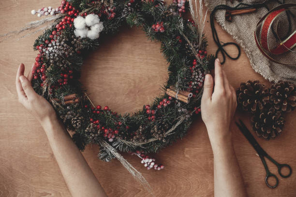 istock Hands holding fir branches, red berries and pine cones,thread, scissors, cinnamon, cotton on rustic wooden background. Rustic Christmas wreath flat lay. Making  wreath at workshop 1075044840