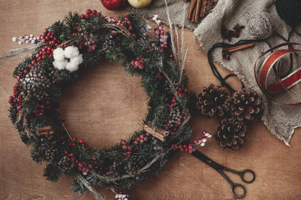 istock Rustic Christmas wreath, flat lay. Fir branches with red berries,pine cones,ribbon, scissors, cinnamon, cotton, apples on rustic wooden background. Atmospheric moody image 1075045260