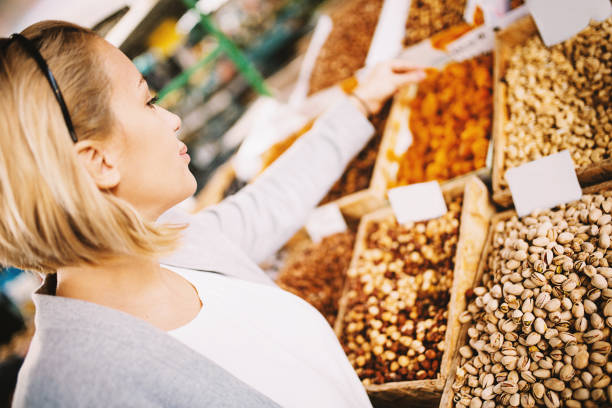 Beautiful blonde woman buying dried apricots at food market.
