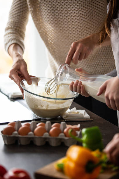 Mother and daughter baking cookies Girl is helping her mother in the kitchen. She is pouring the milk into a batter while her mother mixes the ingredients. muffin tin eggs stock pictures, royalty-free photos & images