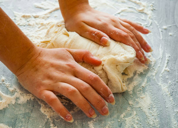 istock Woman's hands knead dough on wooden table 1075062506