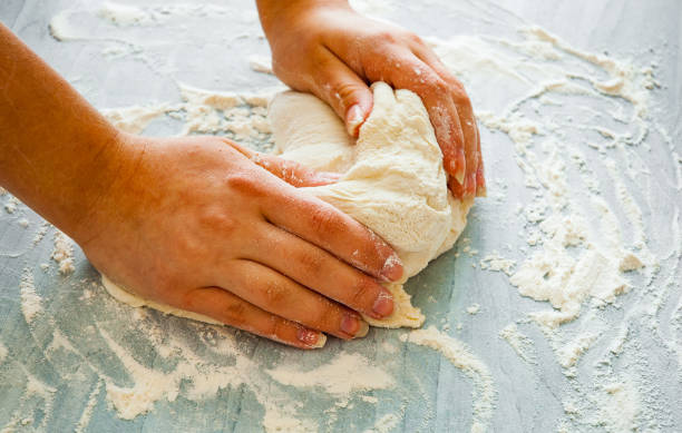 istock Woman's hands knead dough on wooden table 1075063794