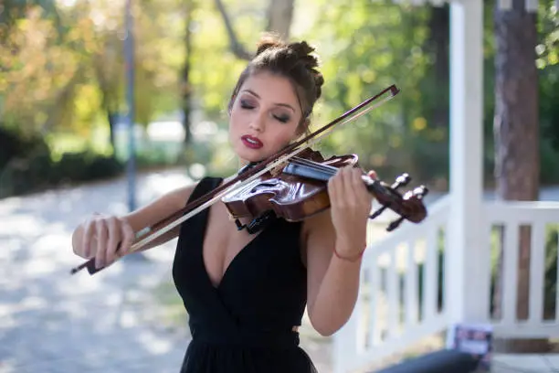 Female violinist playing a violin outdoors in a music pavilion or bandstand. About 25 years old, Caucasian woman.
