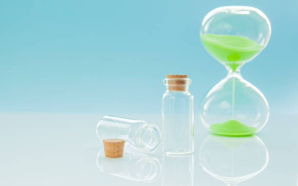 istock Empty little bottles with cork stopper and hourglass on light blue background, close-up 1075073088