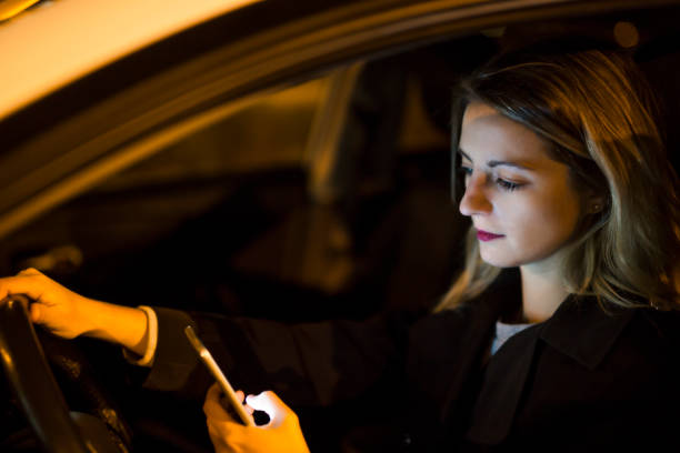 istock Pretty young woman using her smart phone while driving her car at night 1075079544