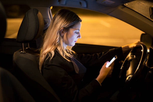 istock Pretty young woman using her smart phone while driving her car at night 1075079612