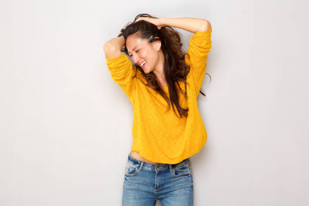 belle jeune femme asiatique, rire avec les mains dans les cheveux contre mur gris - hands behind head photos et images de collection