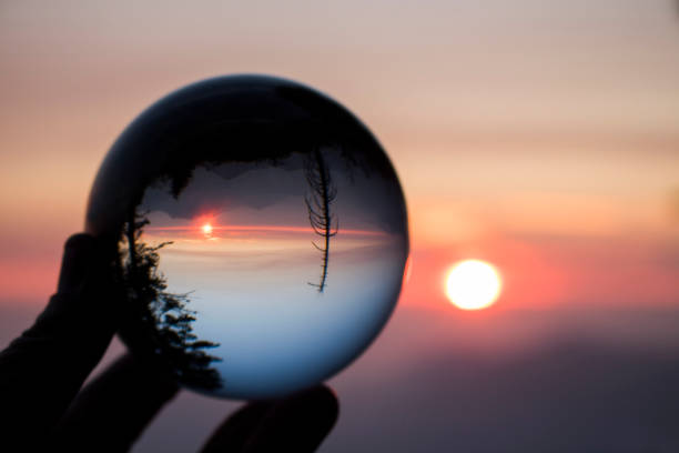 istock Sun Setting on Horizon in Pink and Orange with Mountain Range and Trees in Silhouette Captured In Glass Ball Reflection 1075096148