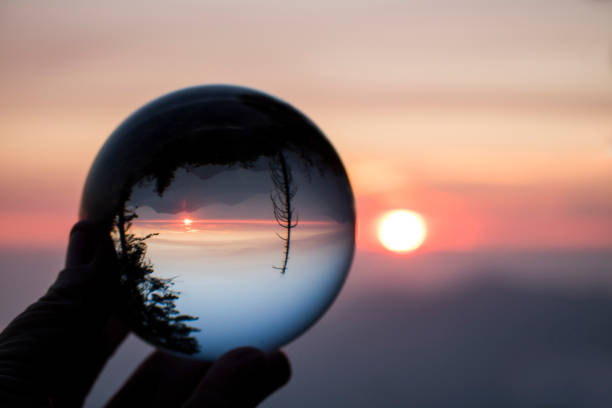 istock Sunset over Mountain Range Captured in Glass Ball Reflection Held in Fingers 1075096150