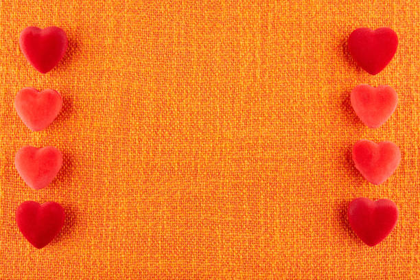 Red velvet hearts lie on orange hessian.