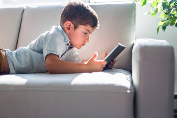 istock Little boy with digital tablet sitting on sofa, on home interior background 1075109992