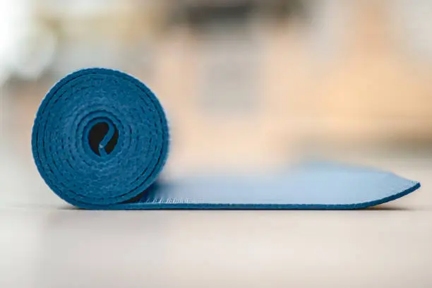A blue yoga mat is slightly unrolled on a wooden floor.