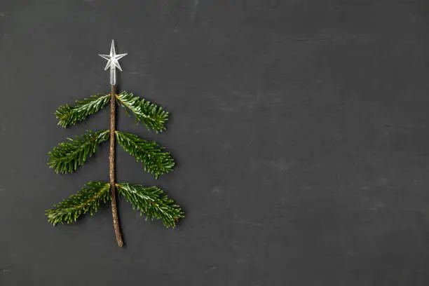 Christmas tree trimming in the shape of a Christmas tree with a star on top on a black rustic wood background with copy space for text.