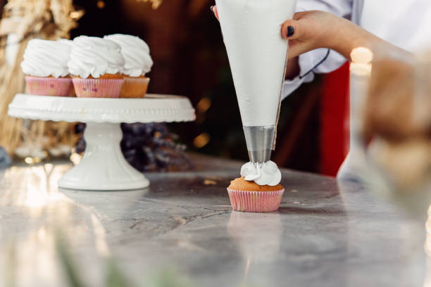 istock female chef with confectionery bag squeezing cream on cupcakes. 1075122918