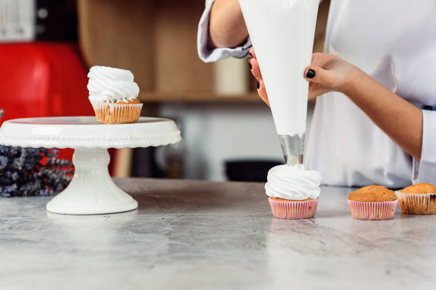 istock female chef with confectionery bag squeezing cream on cupcakes. 1075123006