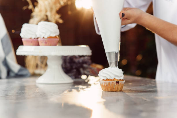 istock female chef with confectionery bag squeezing cream on cupcakes. 1075123028