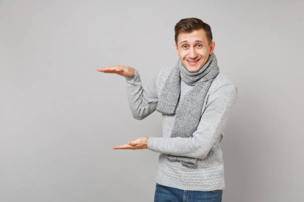 istock Smiling man in gray sweater, scarf gesturing demonstrating size with vertical workspace isolated on grey background. Healthy lifestyle people sincere emotions, cold season concept. Mock up copy space. 1075132666