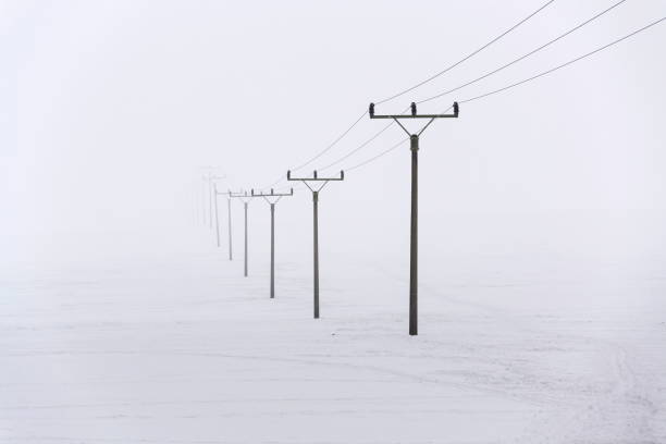 Electricity pylons from distribution power station disappearing in deep fog, winter freezing weather concept stock photo