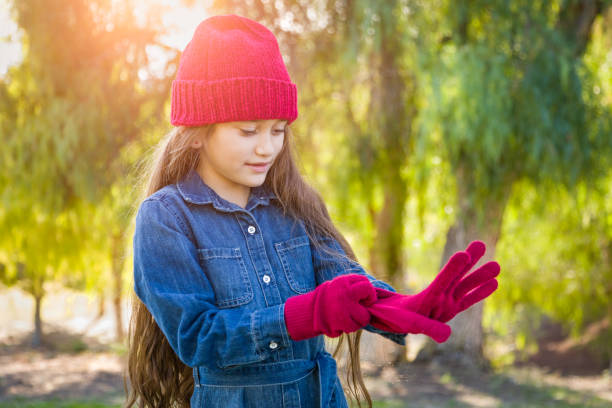 Cute Mixed Race Young Girl Wearing Red Knit Cap Putting On Mittens Outdoors Cute Mixed Race Young Girl Wearing Red Knit Cap Putting On Mittens Outdoors. hot mexican girls stock pictures, royalty-free photos & images