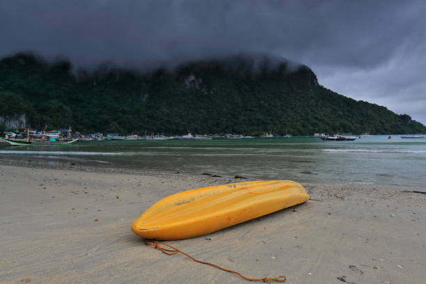 Yellow kayak stranded-fishing and tour boats moored. El Nido beach-Palawan-Philippines-0806 Yellow fiberglass kayak stranded upside down at the beach-tourboats moored in a rainy morning preventing them from going out to sea for fishing and tourist islands hopping. El Nido-Palawan-Philippines fishing boat sinking stock pictures, royalty-free photos & images