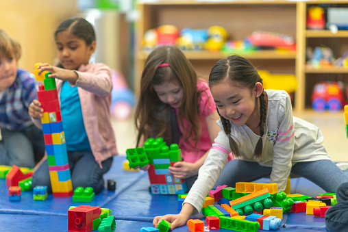 Several kindergarteners are playing with toy building blocks in their classroom.