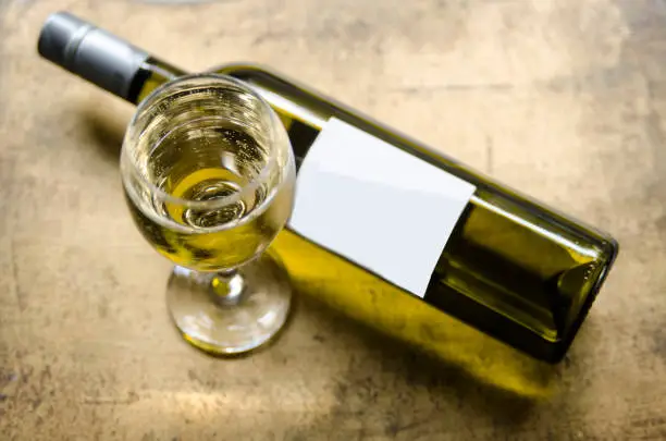 Photo of White wine in glass and bottle on golden rustic table