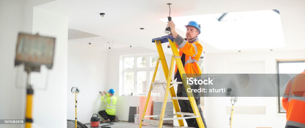 electric house rewire electrician installing downlights Electrician Stock Photo